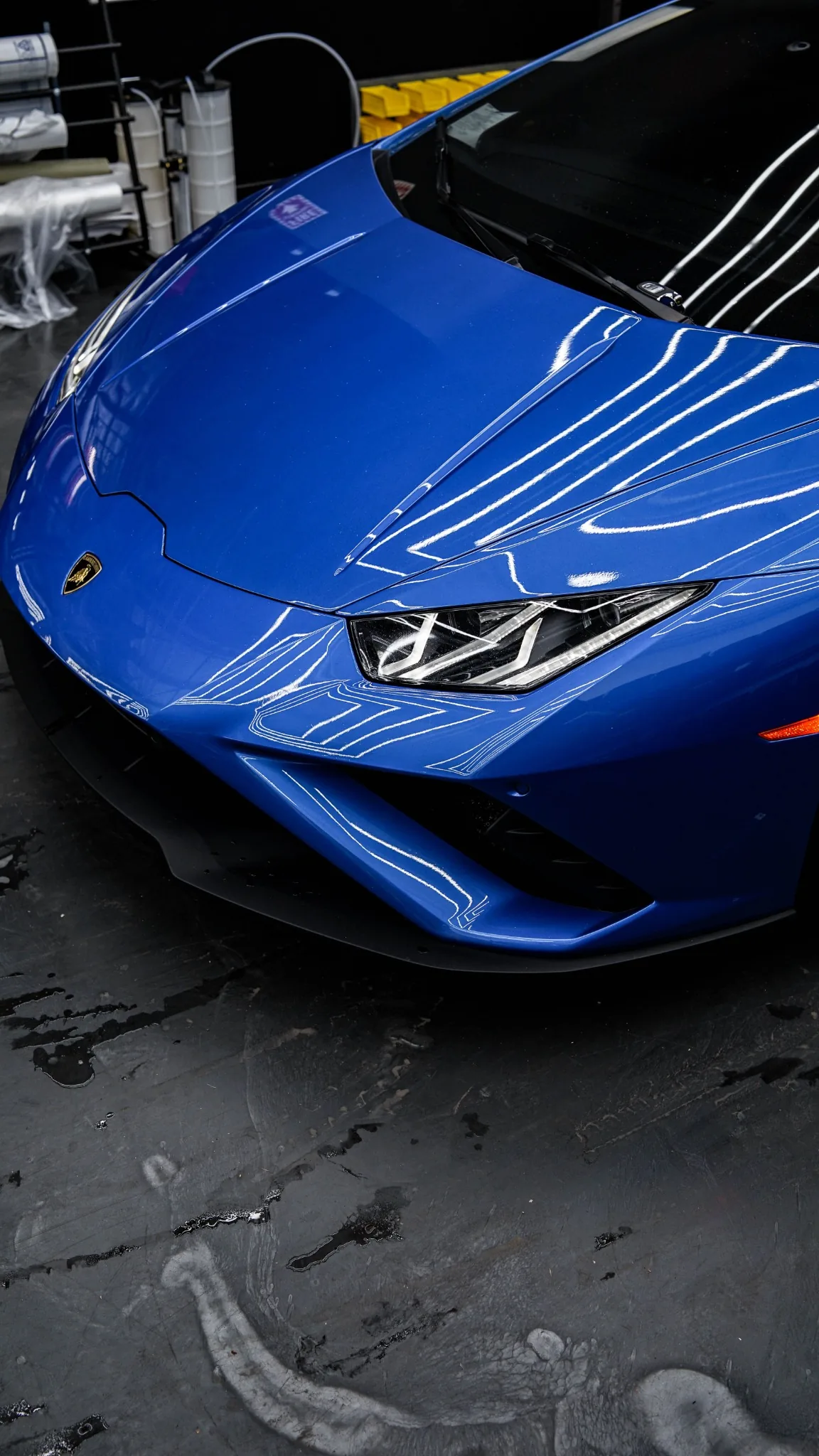 A blue Lamborghini with glossy paint reflecting the workshop lights